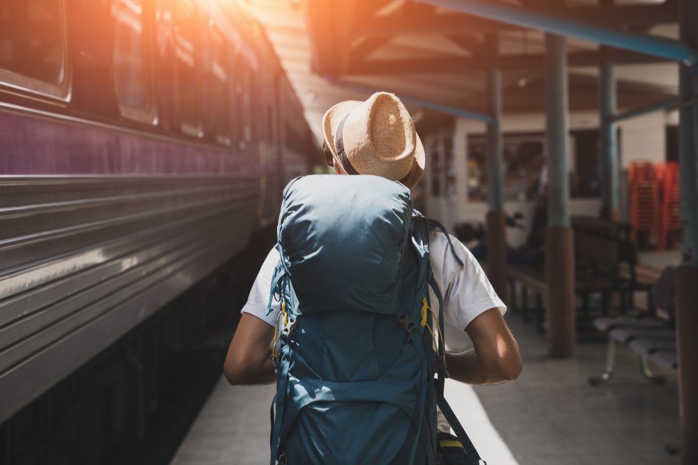 Male traveler with backpack walking next to a train he needs to catch