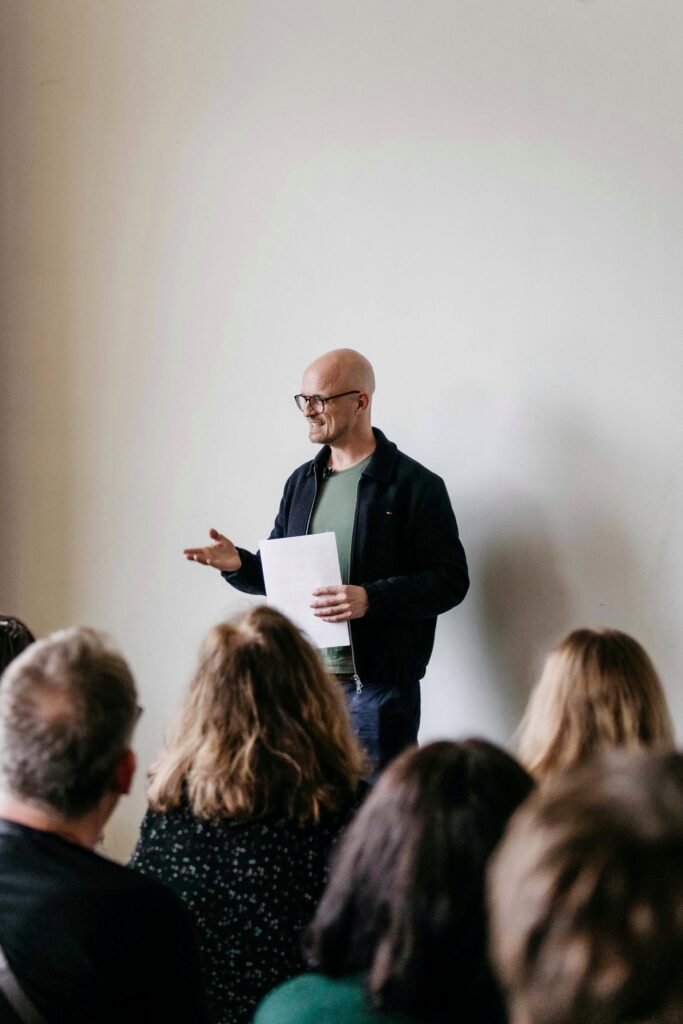 Christian Hansen speaks in front of an audience, holding the manuscript of his short story he will shortly be reading.